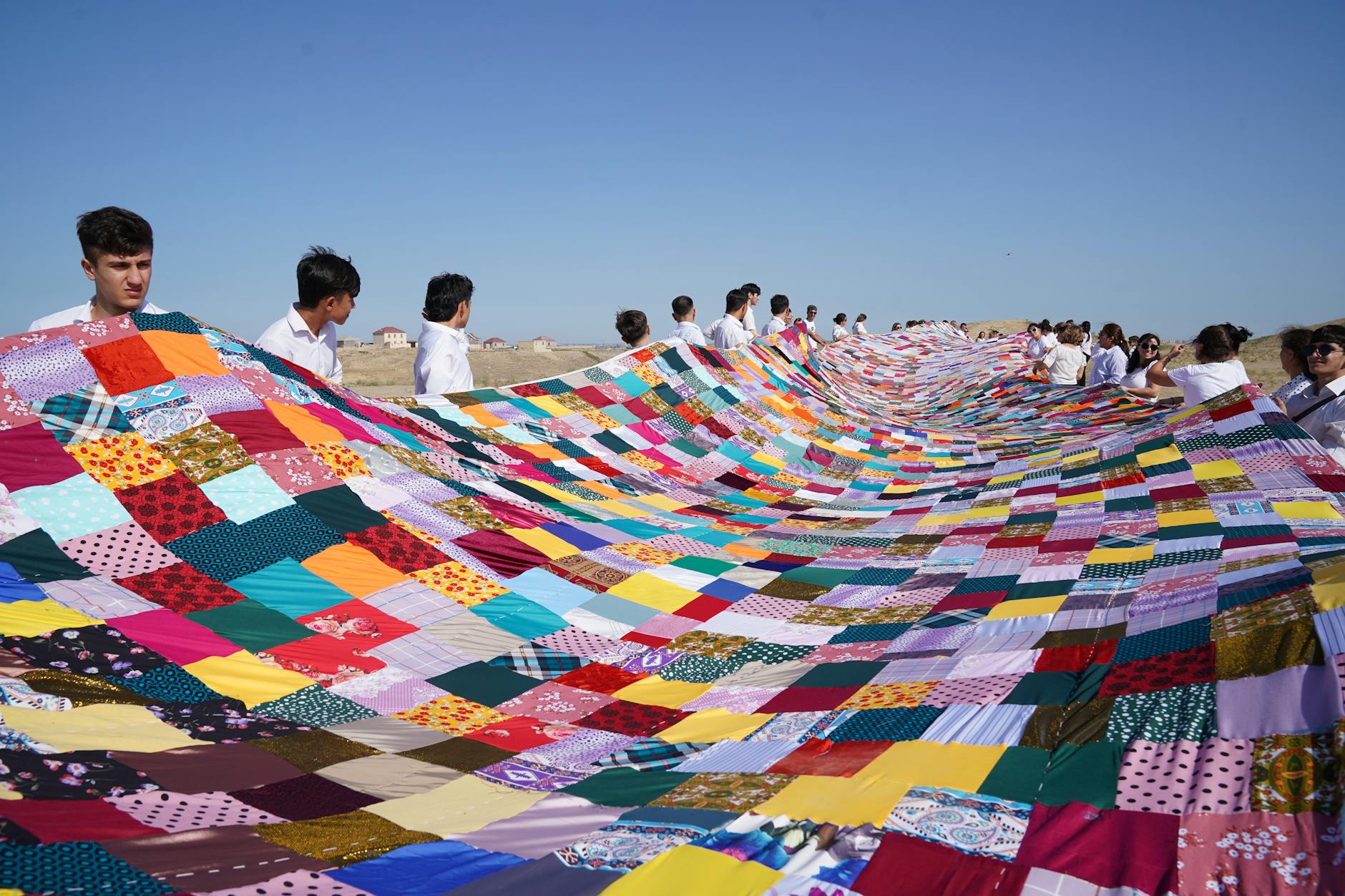 colorful patchwork quilt held by group outdoors